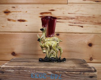 Może przedstawiać: Ceramiczny wazon z burgundowym szkliwem i wzorem dwóch jeleni. Wazon stoi na drewnianej powierzchni.