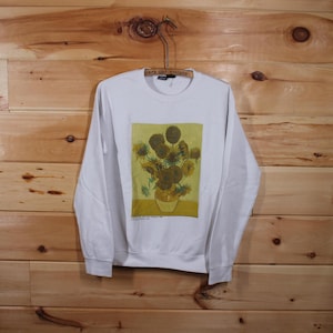 Puede incluir: Sudadera blanca de manga larga con un estampado de una pintura de girasoles en un jarrón. La pintura se titula "Girasoles" de Vincent van Gogh.