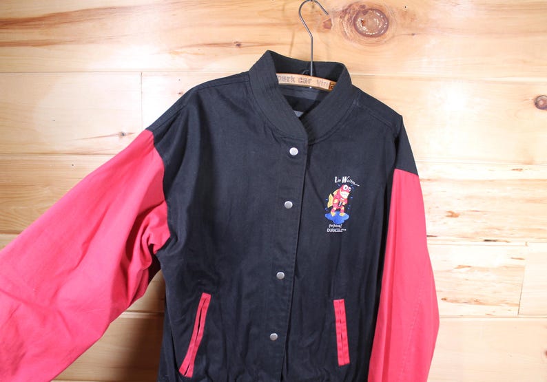 K&ouml;nnte beinhalten: Schwarze und rote Baseballjacke mit einem roten und blauen gestickten Logo eines Comic-Charakters auf der Vorderseite. Das Logo lautet "Le Hibou" und "Planet Dracula".