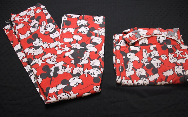 Op de afbeelding: Rode pyjama met een zwart-witte Mickey Mouse print. De pyjama is gevouwen en ligt op een zwarte ondergrond.