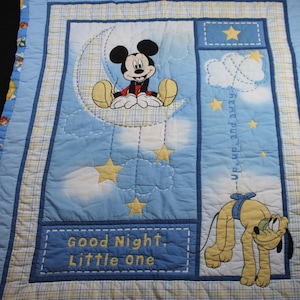 Puede incluir: Edredón para bebé azul y blanco con Mickey Mouse en una luna creciente, Pluto, estrellas y nubes. El edredón tiene bordadas las palabras "Good Night, Little One". Es un artículo de ropa de cama para bebés.
