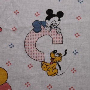 May include: A white fabric with a red and blue polka dot pattern. Mickey Mouse, Pluto, and Donald Duck are featured on the fabric. Mickey Mouse is sitting on a red and white polka dot letter C. Pluto is sitting next to the letter C. Donald Duck is in the upper left corner of the fabric.