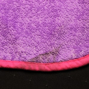Pode incluir: Tecido felpudo roxo e rosa com uma bainha rosa. O tecido tem uma superf&iacute;cie texturizada.