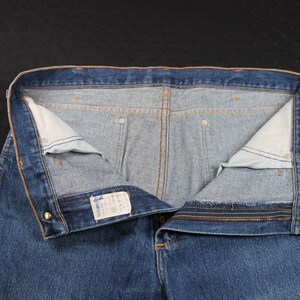 May include: A pair of blue denim jeans with a zipper fly and a button closure. The jeans have a light blue wash and are turned inside out to show the stitching and pockets.