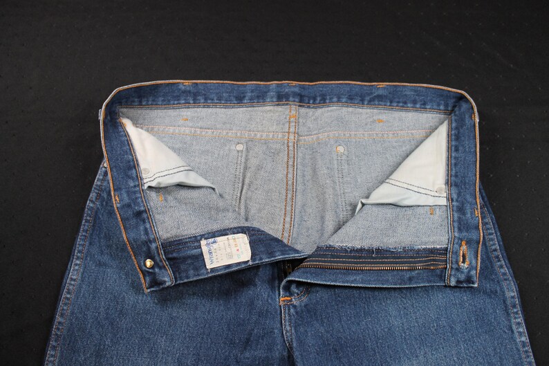 May include: A pair of blue denim jeans with a zipper fly and a button closure. The jeans have a light blue wash and are turned inside out to show the stitching and pockets.