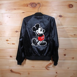 May include: Black satin bomber jacket with a large embroidered Mickey Mouse design on the back. The design features Mickey Mouse in his classic red shorts and yellow shoes.