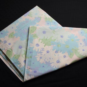 Puede incluir: Un trozo de tela doblado con un patrón floral en tonos de azul, verde y blanco. La tela tiene un tacto suave y delicado y es perfecta para proyectos de manualidades o costura.