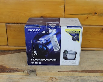 May include: A rectangular cardboard box for a Sony Handycam DCR-DVD108 NTSC camcorder. The box features a dark blue and white color scheme with product imagery, including a close-up of the lens and a full view of the silver camcorder.