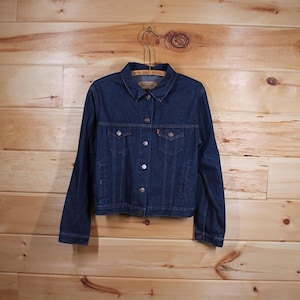 Op de afbeelding: Een donkerblauw denim jack met knoopsluiting en twee voorzakken. Het jack heeft een Levi's label op de zak.