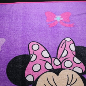 Pode incluir: Cobertor de l&atilde; roxo com um la&ccedil;o rosa com bolinhas brancas, orelhas pretas e um rosto bronzeado. O cobertor tamb&eacute;m tem um la&ccedil;o rosa com uma flor azul no centro e um cora&ccedil;&atilde;o rosa no canto superior esquerdo.