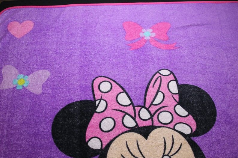Pode incluir: Cobertor de l&atilde; roxo com um la&ccedil;o rosa com bolinhas brancas, orelhas pretas e um rosto bronzeado. O cobertor tamb&eacute;m tem um la&ccedil;o rosa com uma flor azul no centro e um cora&ccedil;&atilde;o rosa no canto superior esquerdo.