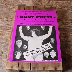 Könnte beinhalten: Eine Vintage-Ausgabe des Magazins Body Press mit einem Wrestler, Andre the Giant, auf dem Cover. Das Magazin hat einen pinkfarbenen Rand und den Titel "BODY PRESS" in großen, fetten Buchstaben. Das Cover enthält auch den Text "OFFICIAL U.S. WRESTLING MAGAZINE".