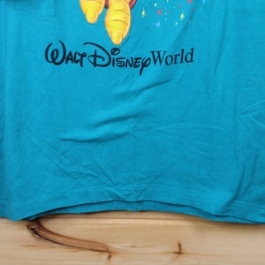 May include: A turquoise blue t-shirt with a cartoon character and the text "Walt Disney World" printed on the front.