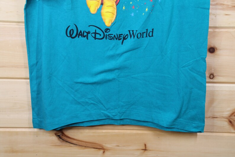 May include: A turquoise blue t-shirt with a cartoon character and the text "Walt Disney World" printed on the front.