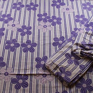 Op de afbeelding: Paarse en witte bloemenstof met een gestreepte achtergrond. De stof is dubbelgevouwen en het patroon is aan beide kanten zichtbaar.