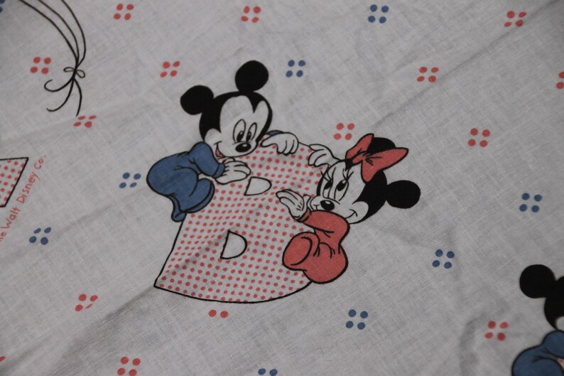 May include: A white fabric with red and blue polka dots. Mickey Mouse and Minnie Mouse are holding a red and white polka dot letter B. The text "The Walt Disney Co." is in the bottom left corner.