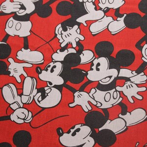 Op de afbeelding: Rode stof met een herhalend patroon van zwarte en witte Mickey Mouse-figuren. De figuren staan in verschillende poses, waaronder zwaaien, glimlachen en hun handen omhoog houden.