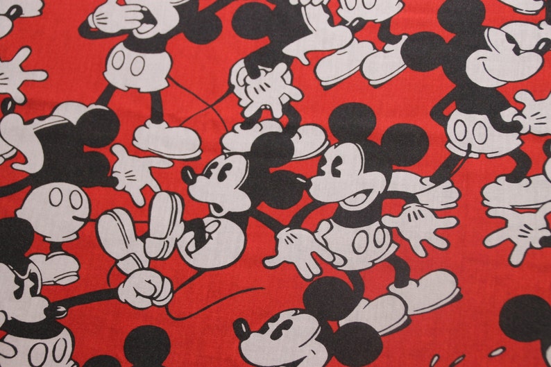 Op de afbeelding: Rode stof met een herhalend patroon van zwarte en witte Mickey Mouse-figuren. De figuren staan in verschillende poses, waaronder zwaaien, glimlachen en hun handen omhoog houden.