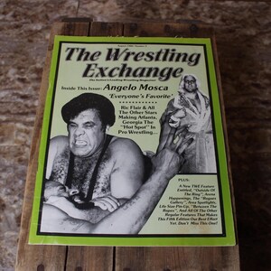Könnte beinhalten: Eine Vintage-Ausgabe des Magazins "The Wrestling Exchange" mit Angelo Mosca auf dem Cover. Das Magazin hat einen grünen Rand und enthält Texte über Wrestling-Stars und -Veranstaltungen. Das Magazin wird auf einer Holzoberfläche angezeigt.