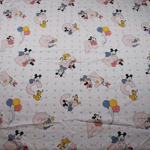 May include: A white baby blanket with a repeating pattern of Mickey Mouse, Minnie Mouse, Donald Duck, and Pluto. The characters are holding balloons and letters of the alphabet. The background is a light blue with small white dots.