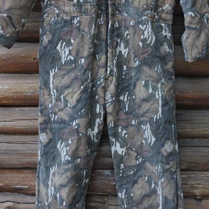 Puede incluir: Mono con estampado de camuflaje y cierre de cremallera. La prenda de una pieza presenta un dise&ntilde;o de hojas marrones, verdes y blancas. El mono de manga larga est&aacute; hecho de una tela duradera, adecuada para actividades al aire libre.