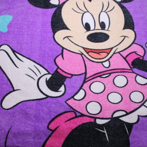 Pode incluir: Uma toalha roxa com uma imagem de desenho animado do Mickey Mouse vestindo um vestido rosa com bolinhas brancas. O Mickey Mouse est&aacute; sorrindo e tem uma luva branca na m&atilde;o esquerda.