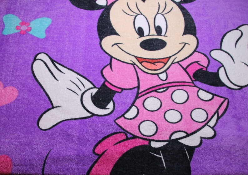 Pode incluir: Uma toalha roxa com uma imagem de desenho animado do Mickey Mouse vestindo um vestido rosa com bolinhas brancas. O Mickey Mouse est&aacute; sorrindo e tem uma luva branca na m&atilde;o esquerda.