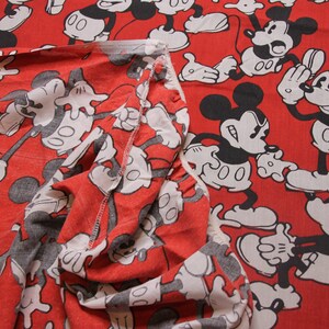 Op de afbeelding: Rode stof met een herhalend patroon van zwarte en witte Mickey Mouse-figuren. De stof is dubbelgevouwen, waardoor het patroon aan beide kanten zichtbaar is.