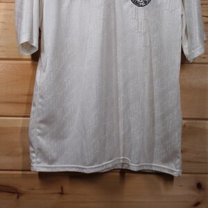 May include: White short-sleeved shirt with a small black and white logo on the front.