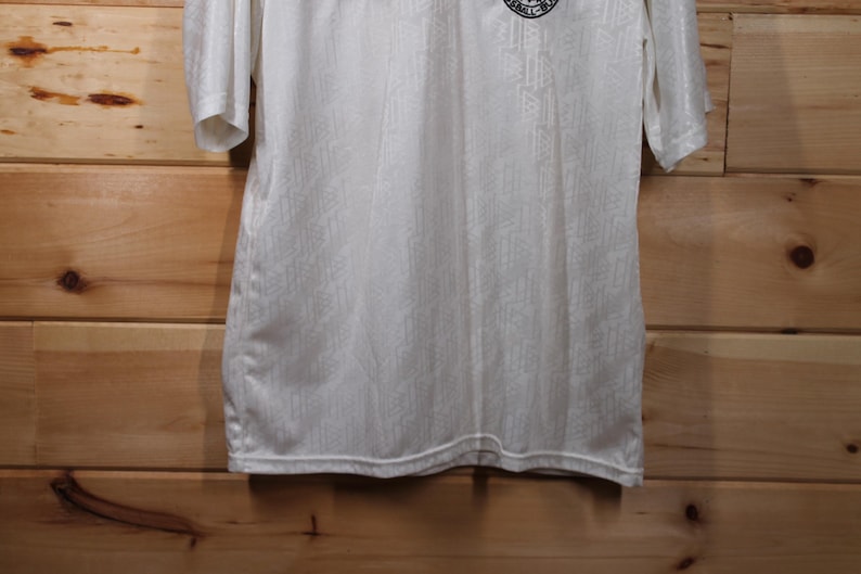 May include: White short-sleeved shirt with a small black and white logo on the front.