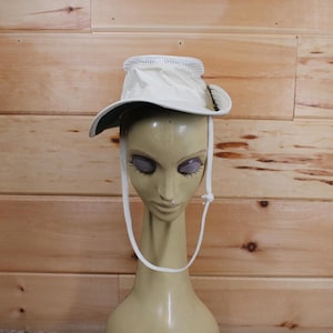 May include: A white sun hat with a green brim and a white chin strap. The hat is on a mannequin head.