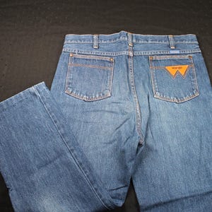 May include: A pair of blue denim jeans with a brown leather patch on the back pocket that says "Wrangler".