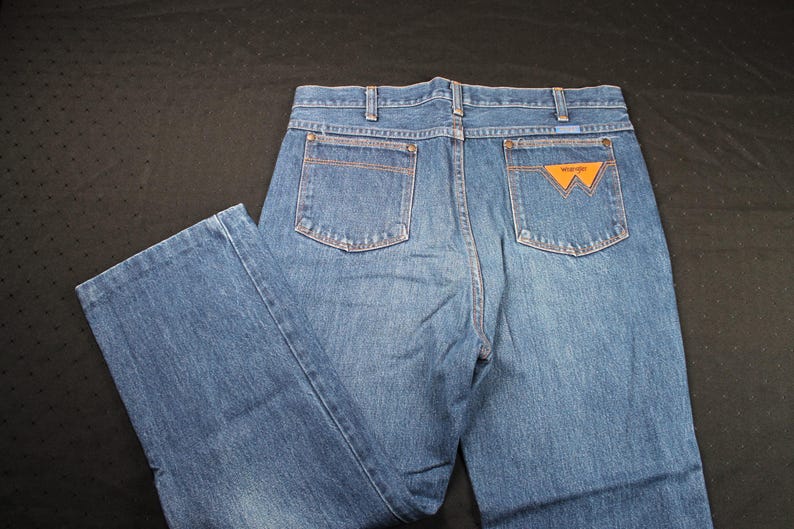 May include: A pair of blue denim jeans with a brown leather patch on the back pocket that says "Wrangler".