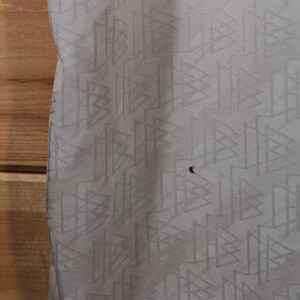May include: White fabric with a repeating geometric pattern of triangles and lines.