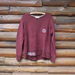 Puede incluir: Sudadera de manga larga color burdeos con un pequeño bolsillo en el lado izquierdo y la palabra "Harvard" impresa en el dobladillo inferior.