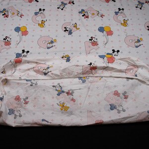 May include: A white fitted sheet with a pink and blue Mickey Mouse and Minnie Mouse print. The sheet features a repeating pattern of Mickey and Minnie Mouse characters holding balloons and letters of the alphabet.