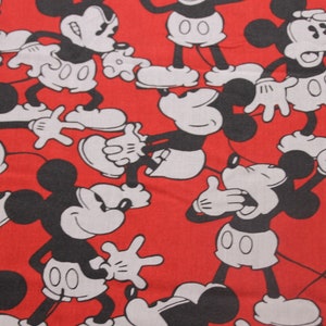 Op de afbeelding: Rode stof met een herhalend patroon van zwarte en witte Mickey Mouse-figuren. De figuren staan in verschillende poses, waaronder zwaaien, glimlachen en verbaasd kijken.