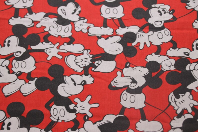Op de afbeelding: Rode stof met een herhalend patroon van zwarte en witte Mickey Mouse-figuren. De figuren staan in verschillende poses, waaronder zwaaien, glimlachen en verbaasd kijken.