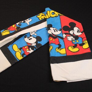 May include: A set of two white cotton towels with a colorful Mickey Mouse design. The towels feature Mickey in various poses against blue and red backgrounds, with black borders and white towel ends.
