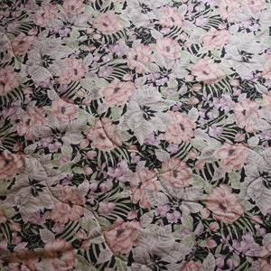 May include: A black fabric with a floral pattern featuring pink, white, and purple flowers. The fabric has a quilted texture.