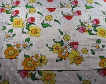 Puede incluir: Dos fundas de almohada blancas con un patrón floral que presenta narcisos amarillos, tulipanes rosas y rojos y margaritas blancas sobre un fondo blanco con pequeños lunares blancos.