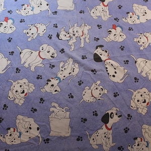 Peut inclure: Un tissu avec un motif répété de chiens dalmatiens de dessin animé dans diverses poses. Les chiens sont blancs avec des taches noires et des colliers rouges, sur fond bleu clair avec des empreintes de pattes noires.
