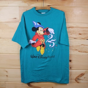 May include: A teal blue t-shirt featuring a cartoon image of Mickey Mouse dressed as a sorcerer, holding a magic wand and a sparkling "25" with the text "Walt Disney World" below.