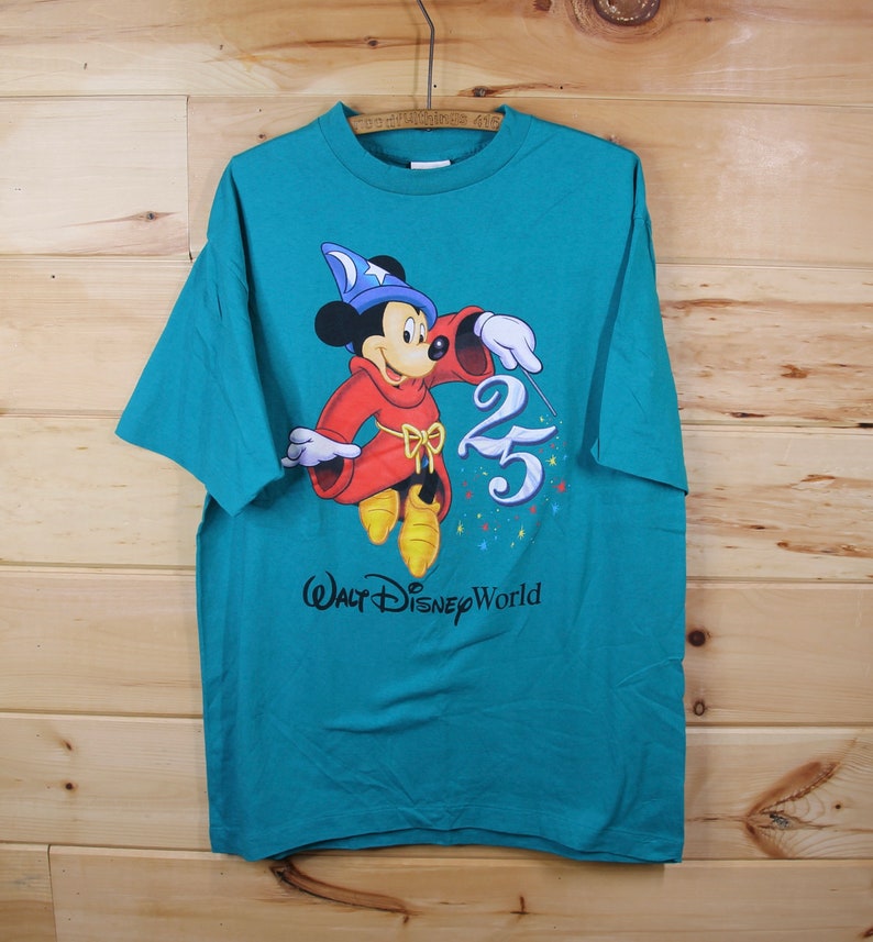 May include: A teal blue t-shirt featuring a cartoon image of Mickey Mouse dressed as a sorcerer, holding a magic wand and a sparkling "25" with the text "Walt Disney World" below.
