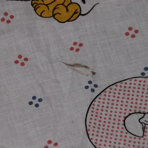 May include: White fabric with red and blue polka dots. A cartoon character is visible in the bottom right corner. The fabric has a small tear.