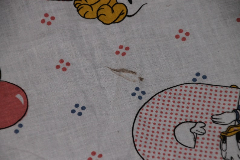 May include: White fabric with red and blue polka dots. A cartoon character is visible in the bottom right corner. The fabric has a small tear.