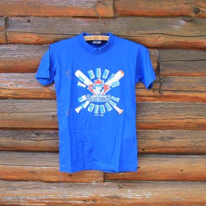 May include: A blue t-shirt featuring a graphic of crossed baseball bats and a maple leaf with the text "Toronto Blue Jays Baseball" printed on the front.