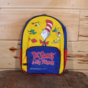 Może przedstawiać: Niebiesko-żółto-czerwony plecak z logo Dr. Seuss & His Friends. Plecak przedstawia kreskówkową postać Kota w Kapeluszu.