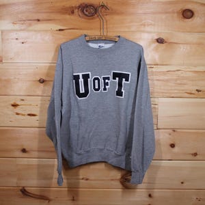 Puede incluir: Sudadera gris con una aplicación de fieltro negro de las letras "U of T" en la parte delantera.