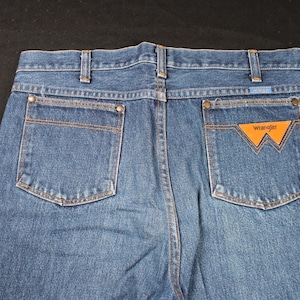 May include: A pair of blue denim jeans with a brown leather patch that says "Wrangler" on the back pocket.